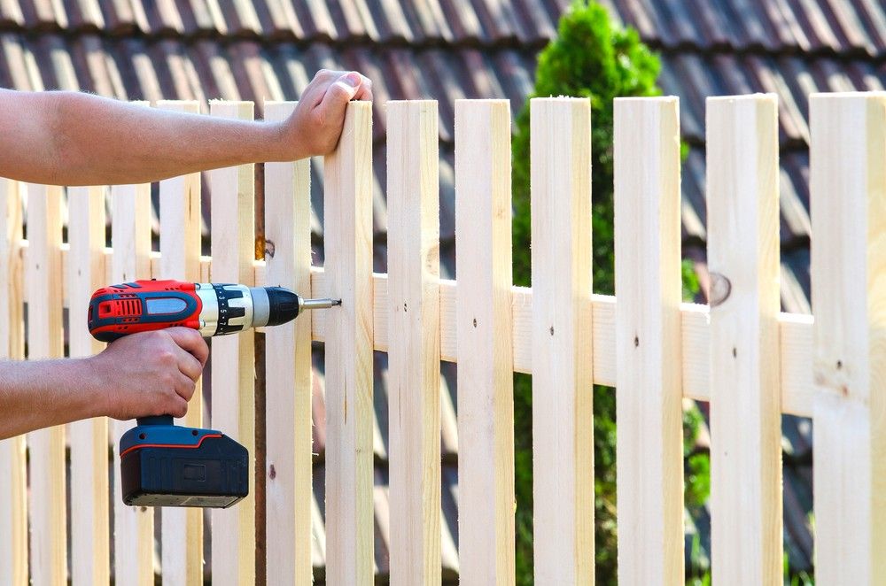 A Person Is Using A Drill To Install A Wooden Fence — CQ Fencing & Retaining Walls In Tannum Sands, QLD