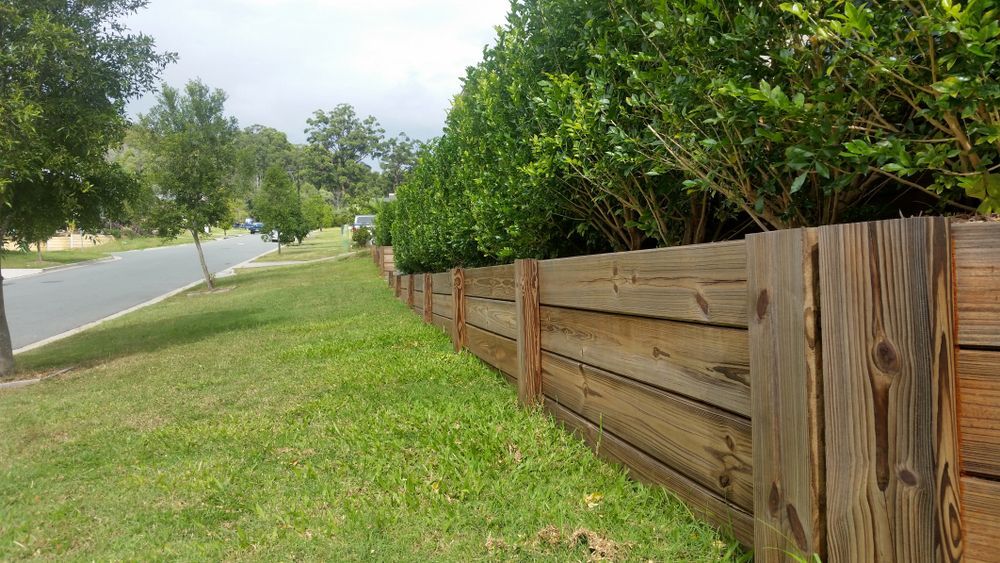 A Blue Picket Fence Surrounds A Brick Wall In A Garden — CQ Fencing & Retaining Walls In Biloela, QLD