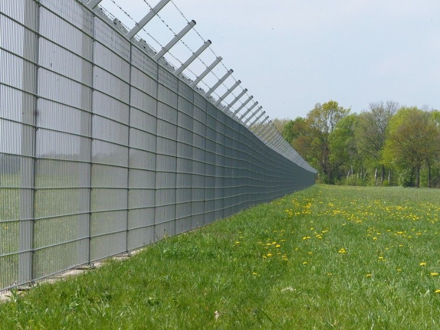 A Fence Surrounds A Grassy Field With Trees In The Background — CQ Fencing & Retaining Walls In Clinton, QLD