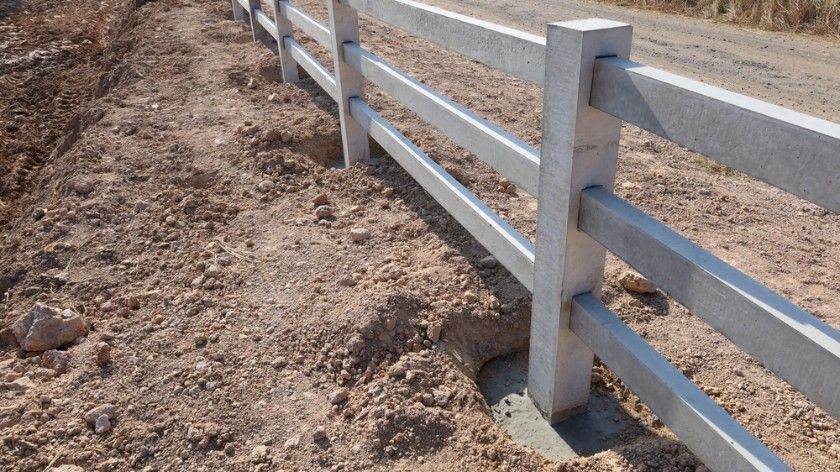 A White Fence Is Sitting On The Side Of A Dirt Road — CQ Fencing & Retaining Walls In Clinton, QLD