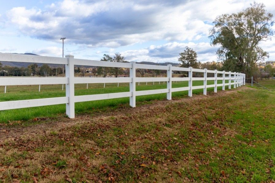 A White Fence Surrounds A Grassy Field With Trees In The Background — CQ Fencing & Retaining Walls In Clinton, QLD