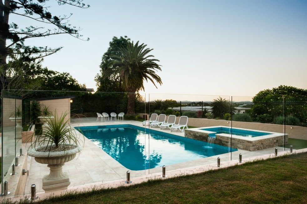 A Large Swimming Pool With A Glass Fence Around It — CQ Fencing & Retaining Walls In Clinton, QLD