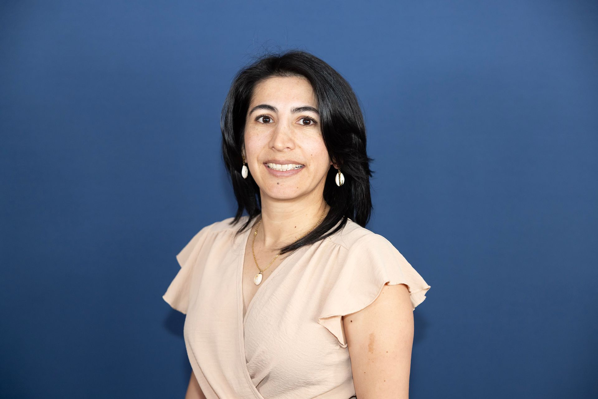 A woman is posing for a picture in front of a blue background.