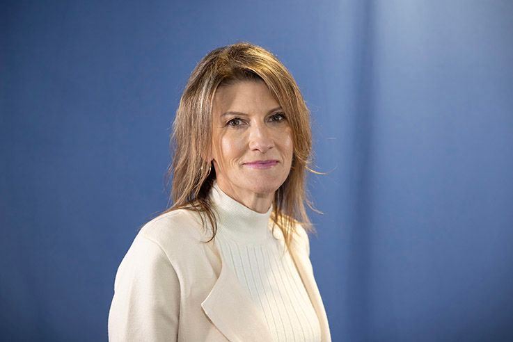 A woman in a pink shirt is smiling in front of a blue background.