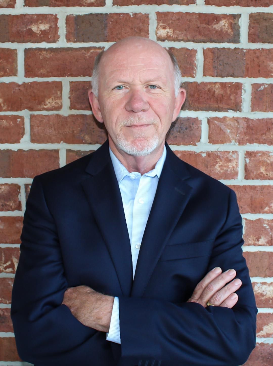 A man with a beard and blue eyes in a grey suit