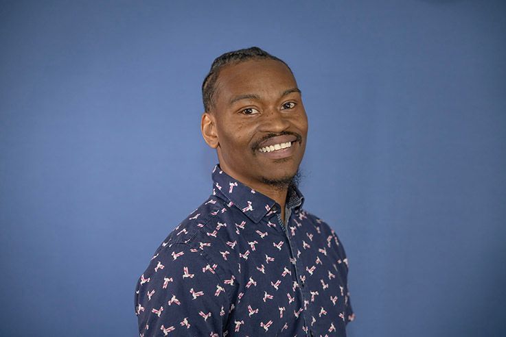 A man in a blue shirt is smiling in front of a blue background.