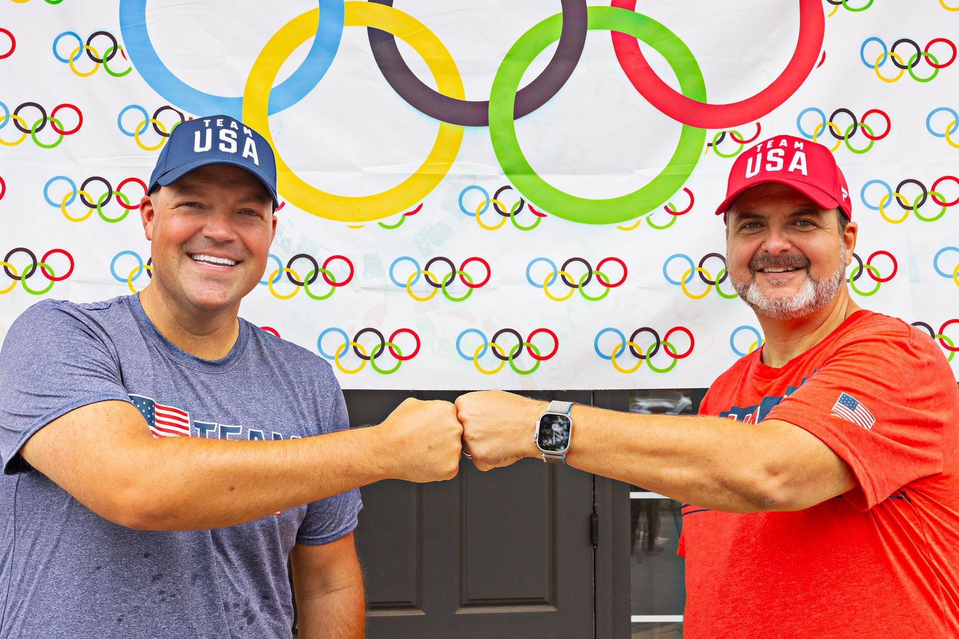 Two men are shaking hands in front of a wall with olympic rings on it.