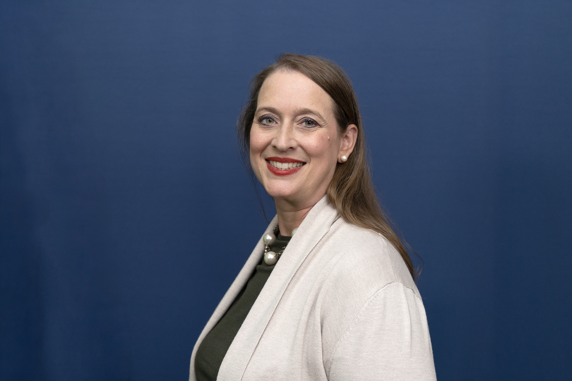 A women with light brown hair wearing a sweater, smiling with a blue background.