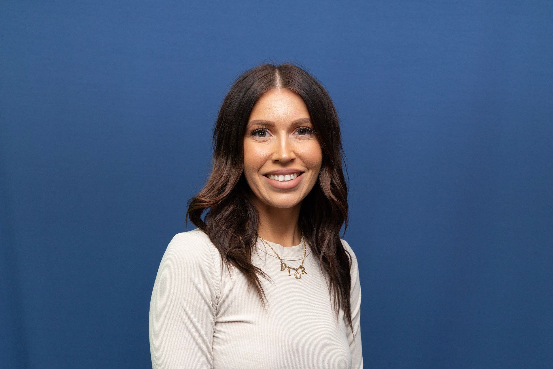 A women with brown hair wearing a sweater, smiling with a blue background.