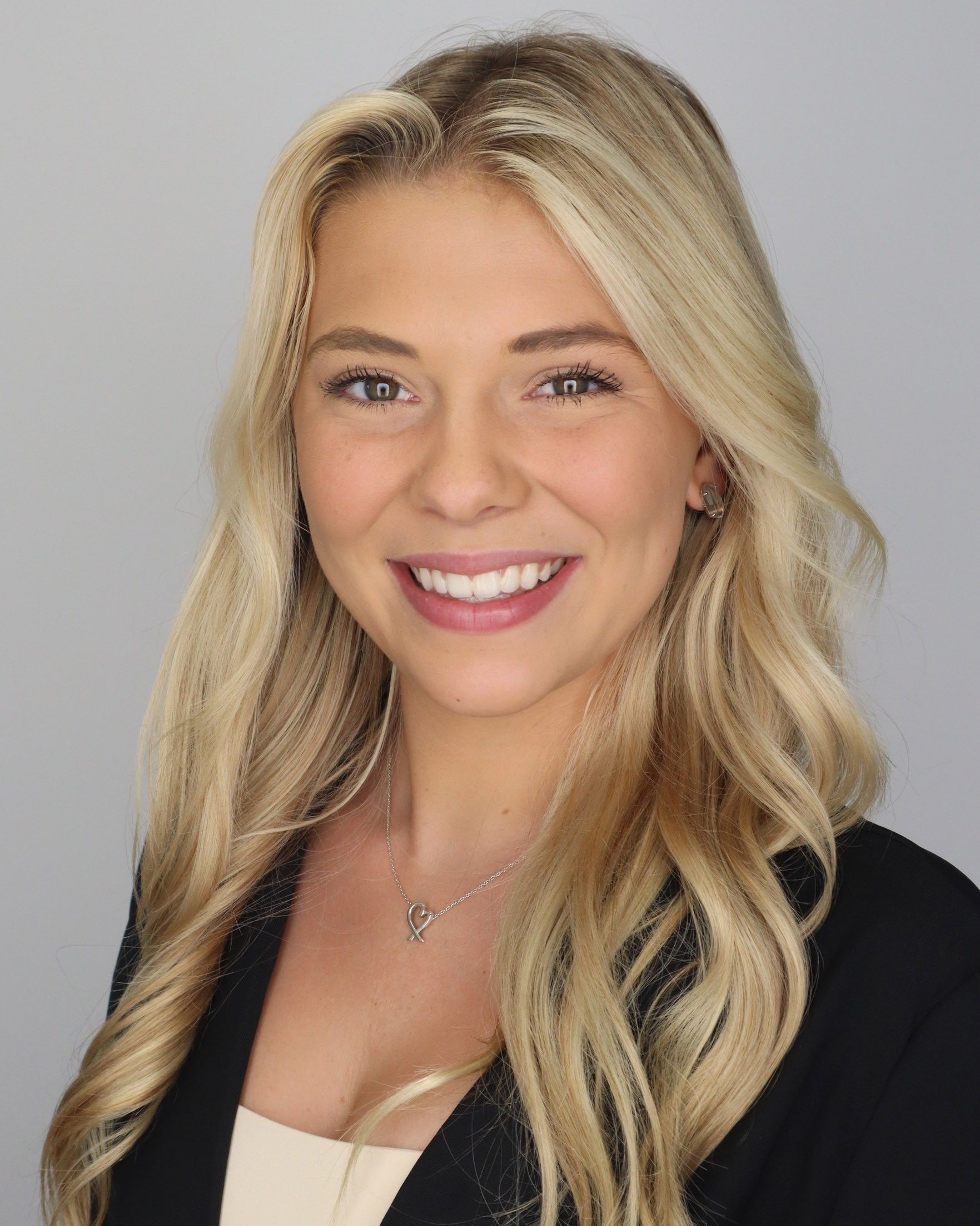 A woman with blonde hair, smiling with a light grey background.