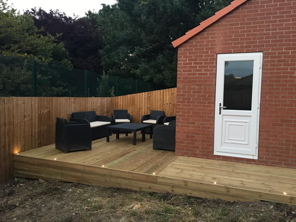 Patio with black outdoor furniture beside a brick house and white door on a wooden deck
