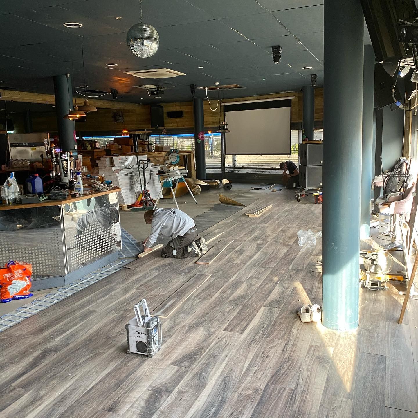 Damaged interior of a café or bar with debris on the floor, tilted tables, and a worker cleaning up.