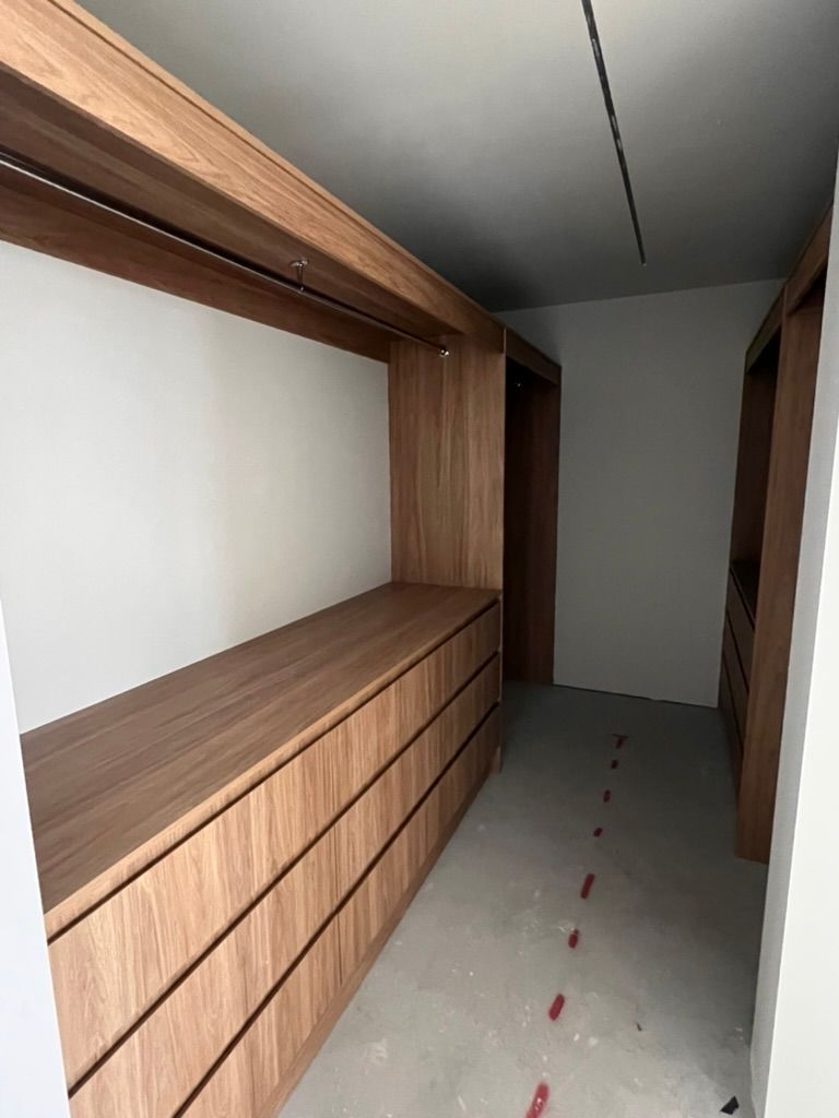 Narrow hallway with built-in wooden drawers and shelving on one side and white walls and floor.