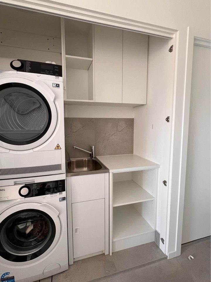 Laundry nook with stacked washer and dryer, sink, and white cabinets with open shelving