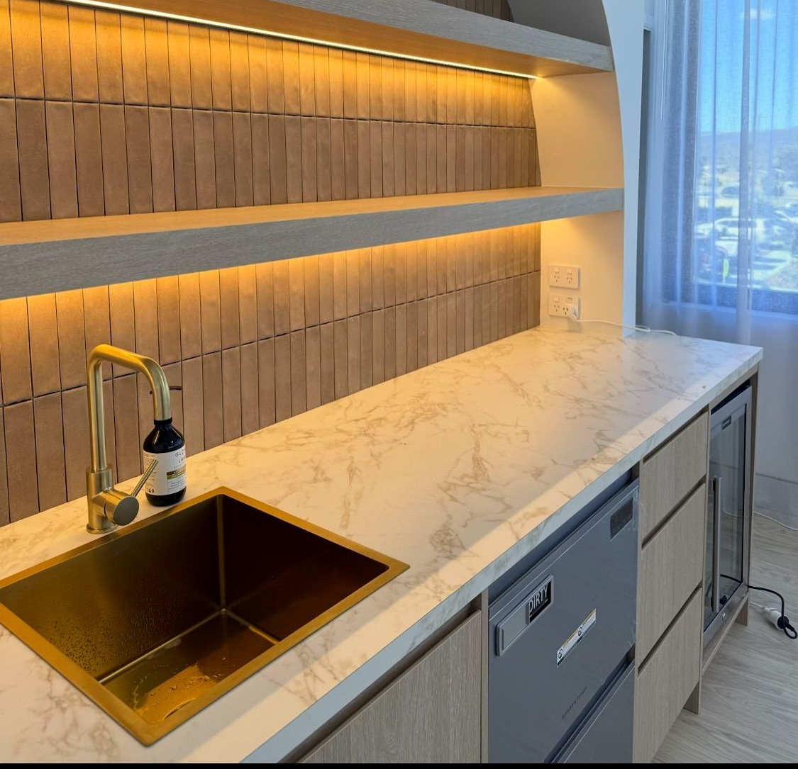 Modern kitchen with marble countertop, copper sink, faucet, under-cabinet lighting, and city view by the window