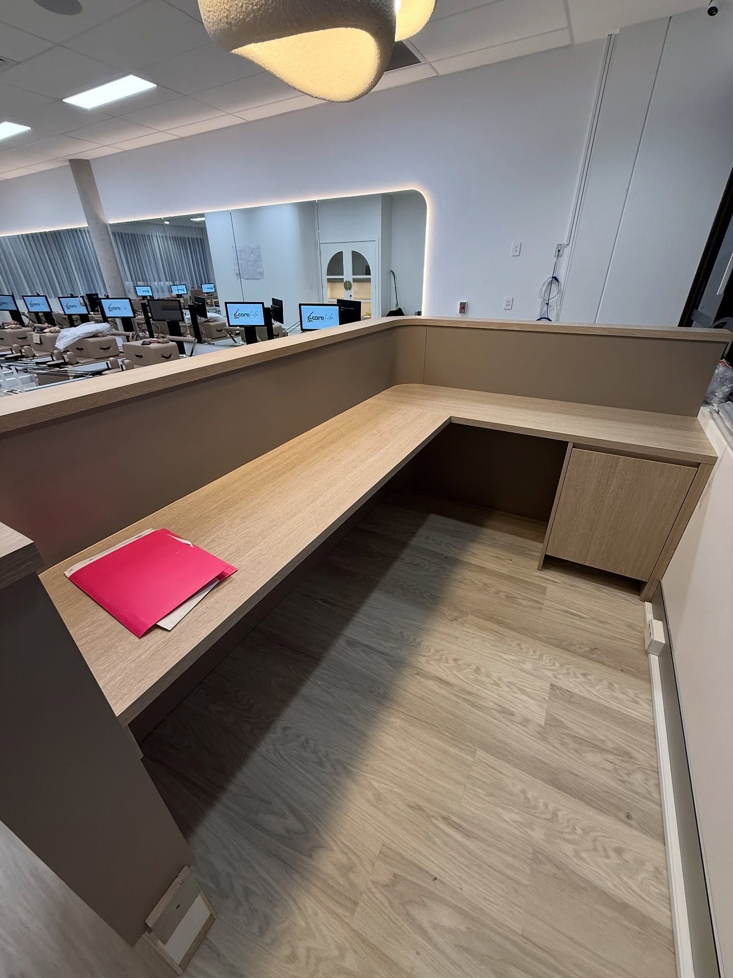 Empty beige office cubicle with built-in desk and a pink folder on the left side of the counter.