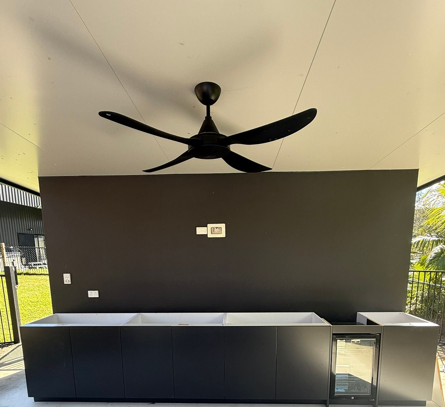 Outdoor covered patio with a black ceiling fan and dark bar counter against a black wall