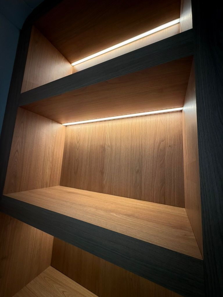 Wooden built-in shelves with warm recessed lighting inside a dark wall niche