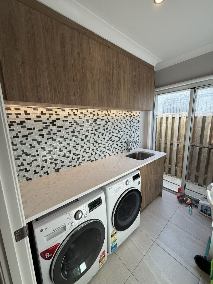 Laundry room with front-load washer and dryer, sink, mosaic backsplash, and sliding glass door to outside