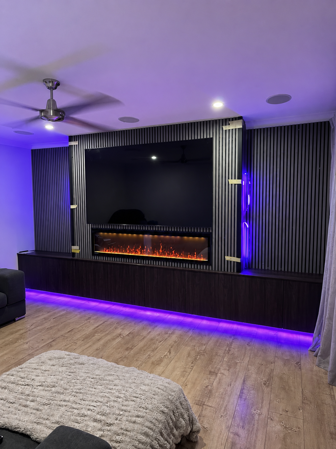 Modern living room with purple LED lighting, electric fireplace, wood floors, and dark accent wall