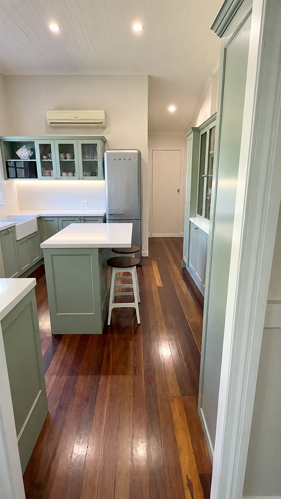 Narrow kitchen with mint green cabinets, white counters, stainless fridge, and wood floors.
