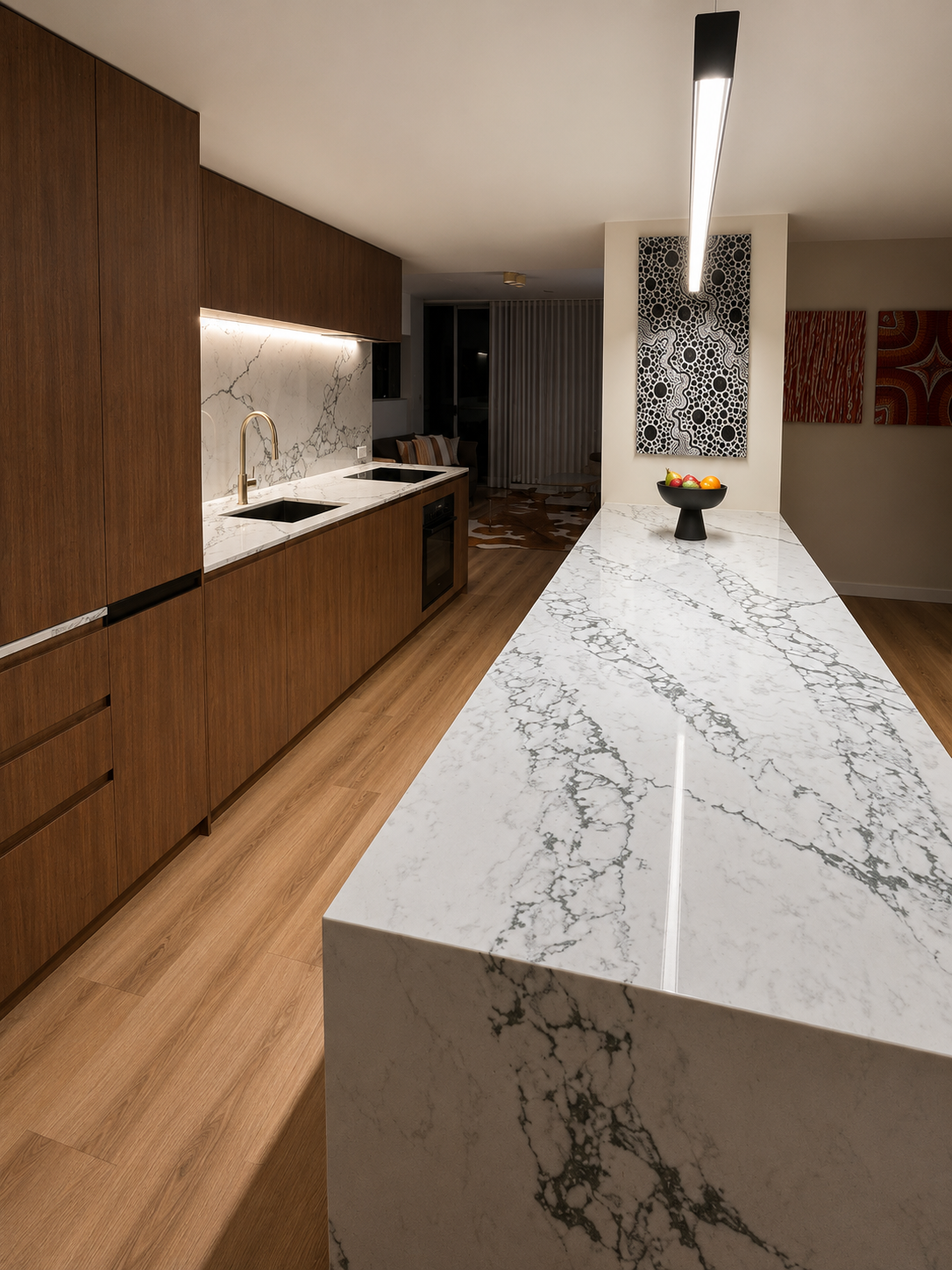 Modern kitchen with wood cabinets, marble island, and long pendant light in a narrow room
