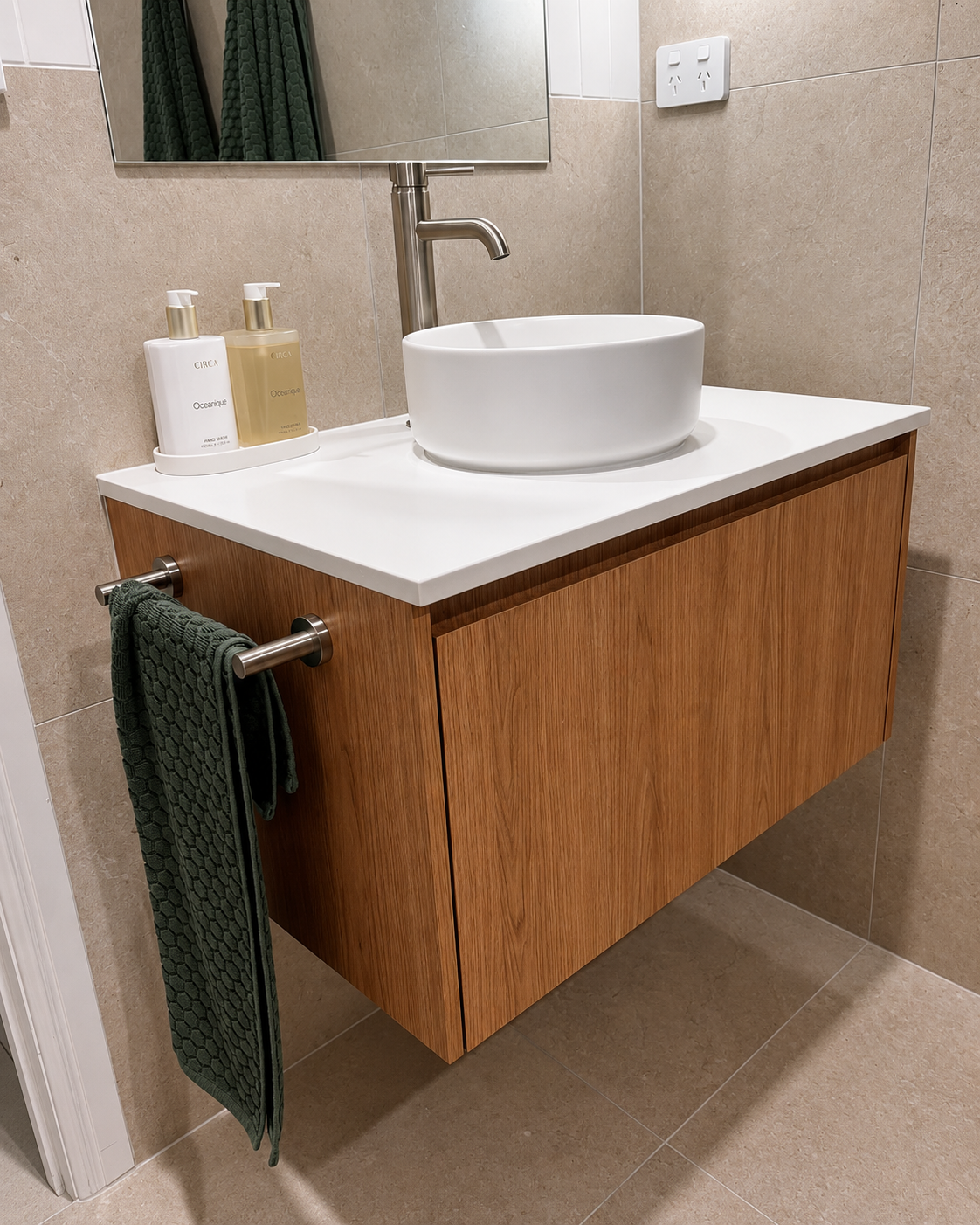 Modern bathroom vanity with white vessel sink, wood cabinet, and green towel