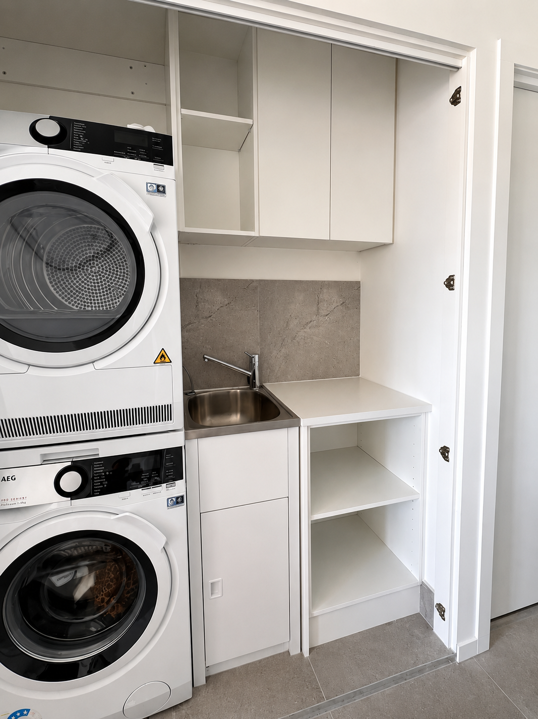 Compact laundry nook with stacked washer and dryer, sink, cabinets, and open shelving