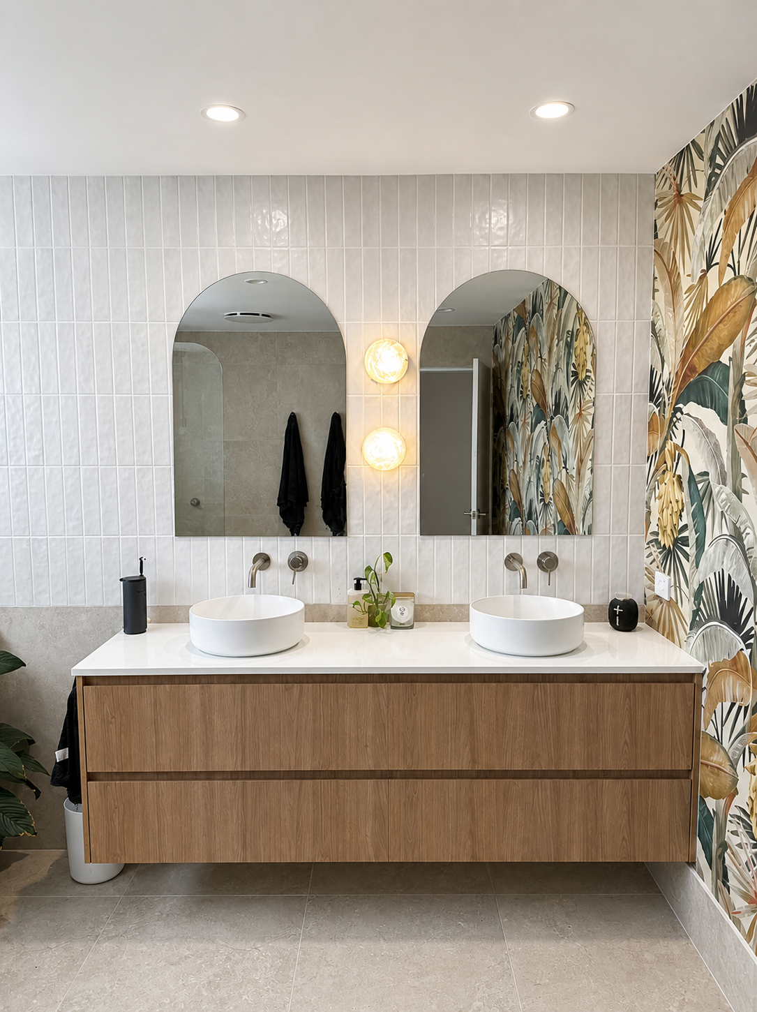 Modern bathroom vanity with double sinks, arched mirrors, and wood cabinets against patterned tile walls