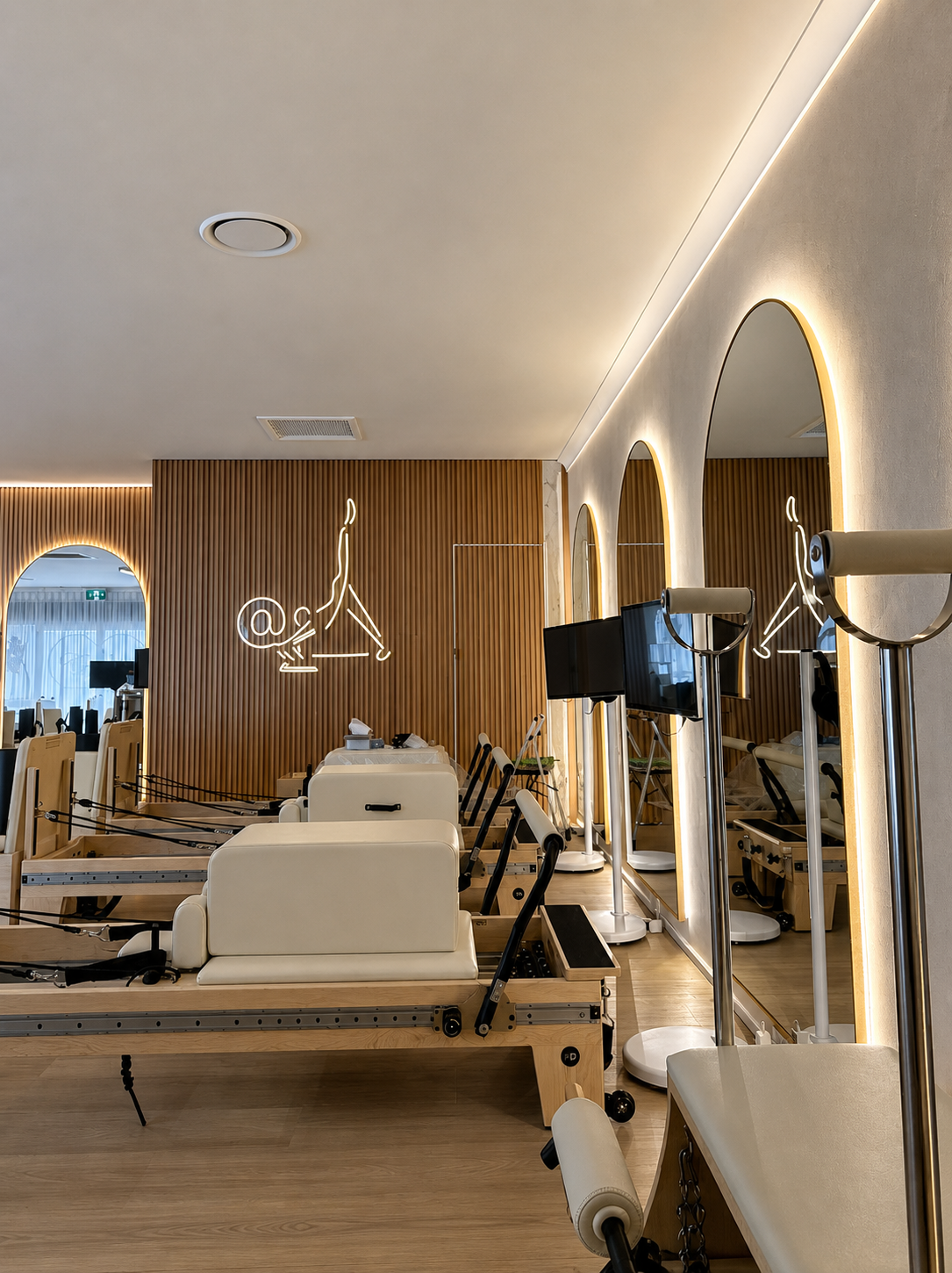 Bright modern Pilates studio with reformer machines, wood slat wall, mirrors, and warm pendant lighting