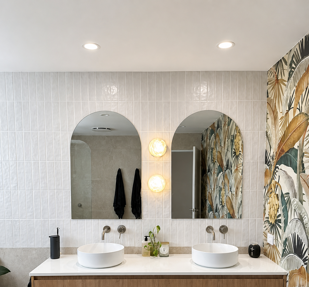 Modern bathroom vanity with two arched mirrors, vessel sinks, white tile, and tropical floral wallpaper accents