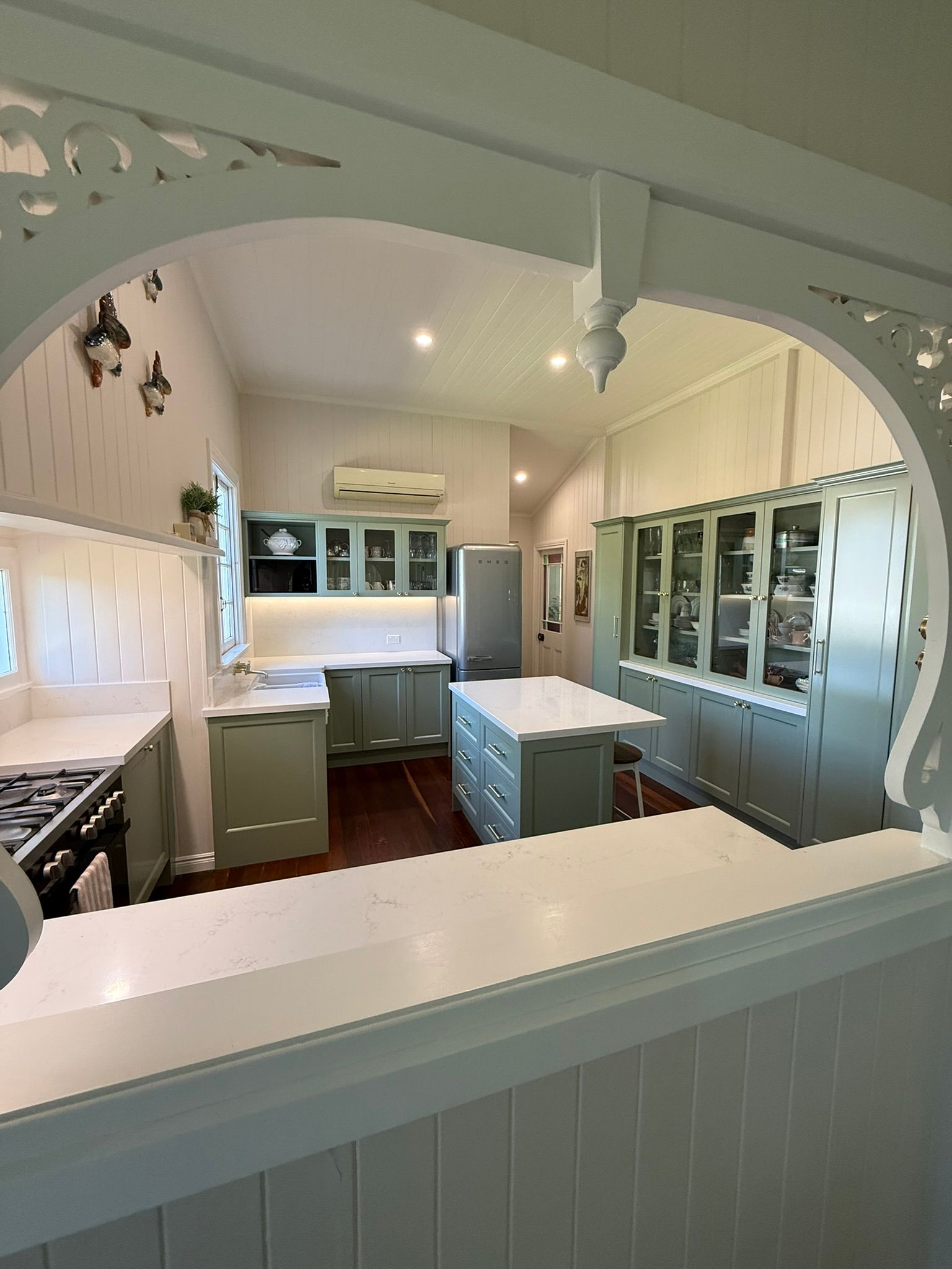 Bright white kitchen with mint cabinets, arched pass-through, and countertop view into the room
