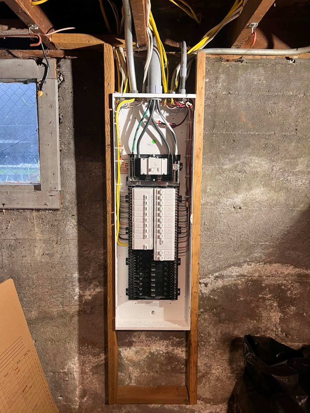 Electrical panel installed in a wooden frame against a gray concrete wall; wires visible above.