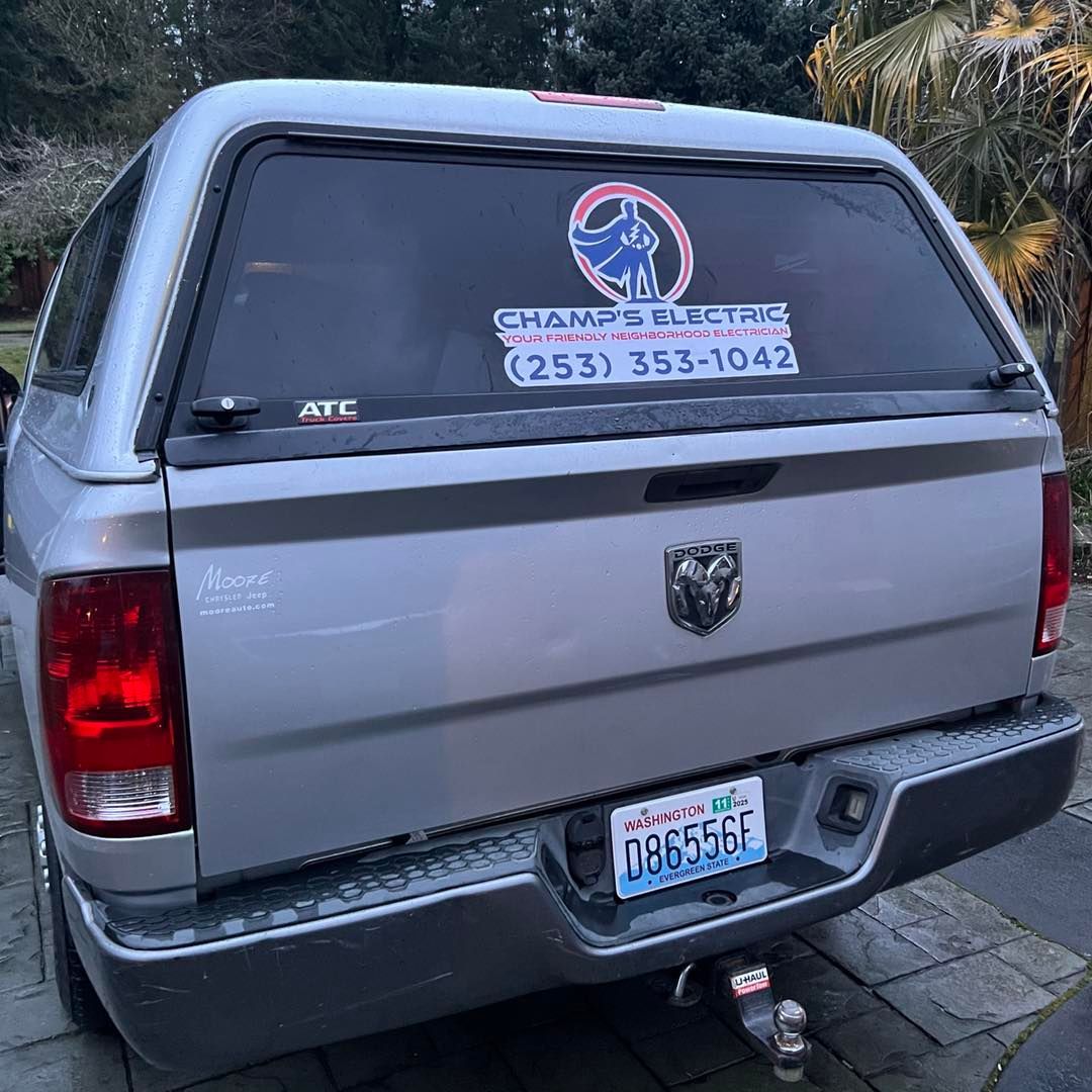 Silver Dodge Ram pickup truck with a camper shell, advertising Champ's Electric.