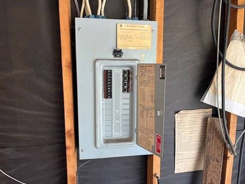 Electrical panel with open door, mounted on wooden supports. Grey panel with breakers.