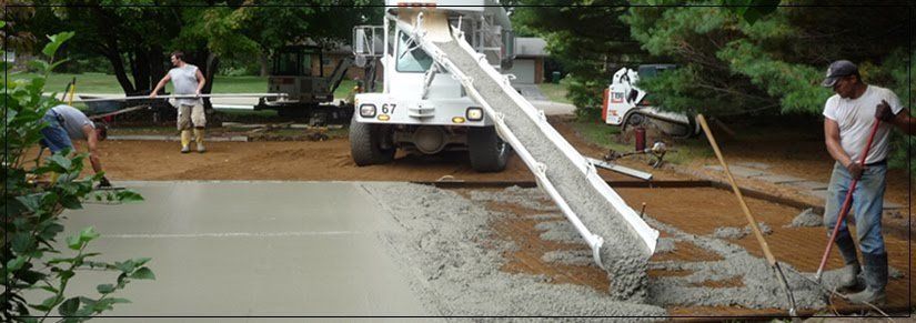 Workers pouring concrete from a truck into a flooded roadway construction site
