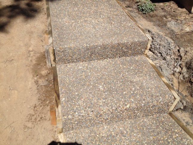 Concrete steps on a dirt path under construction, bordered by rough ground and exposed soil