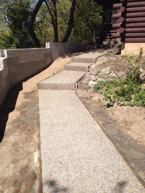 Concrete accessibility path with steps beside a log cabin and stone retaining wall