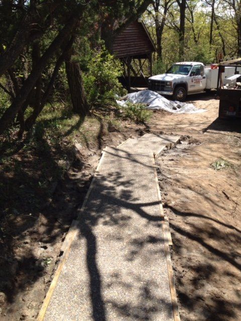 Damaged concrete path in a wooded area beside parked trucks and construction debris