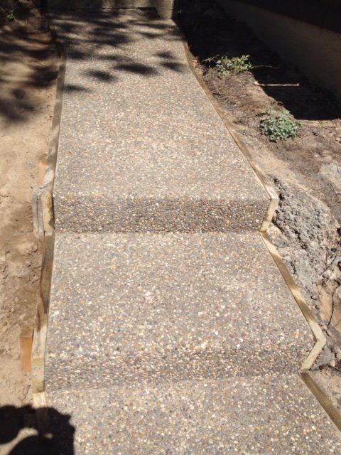 Concrete steps leading up a sloped outdoor path beside a dirt garden bed.
