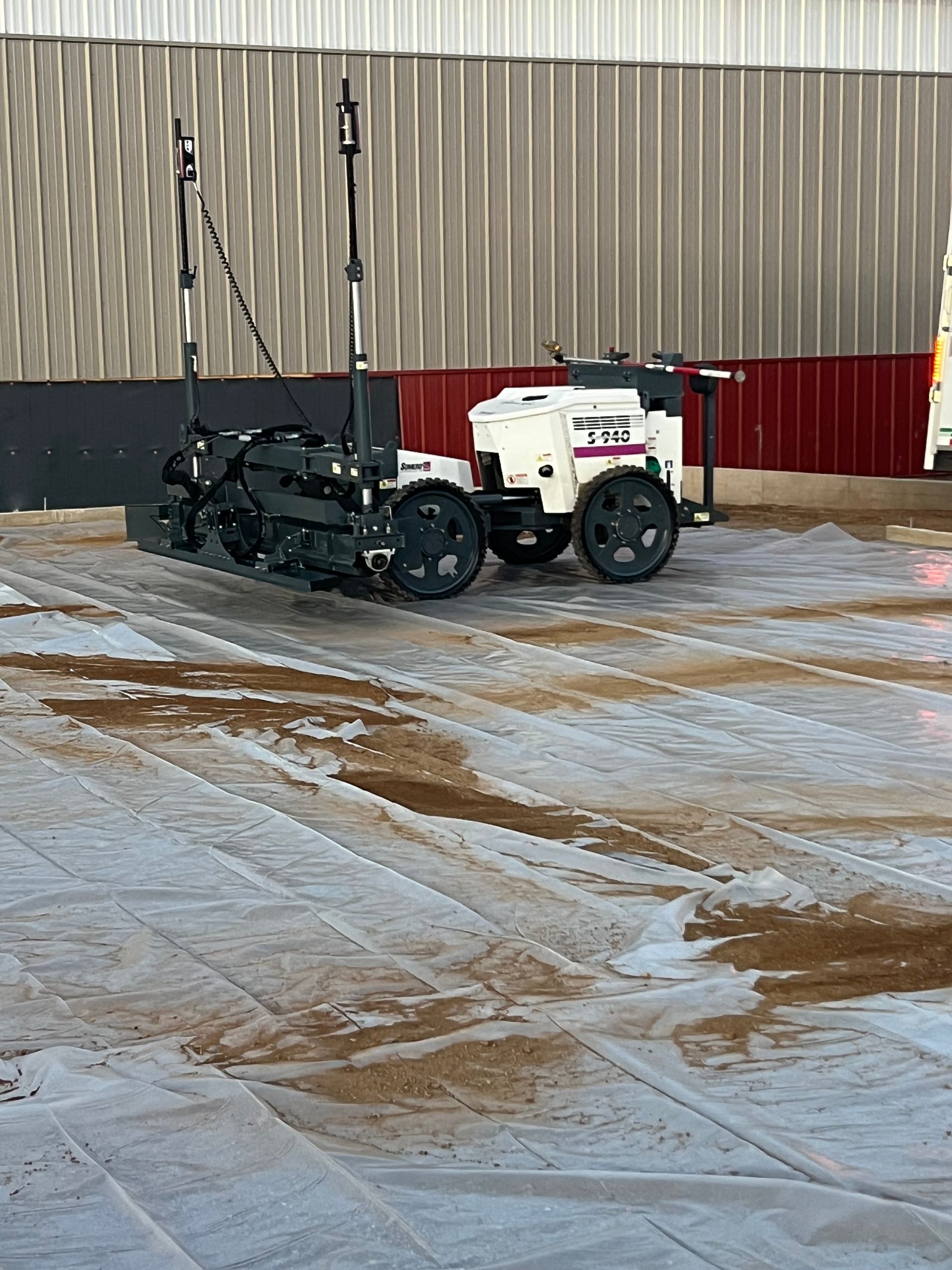 Snow-clearing machine parked on an icy lot beside a large industrial building