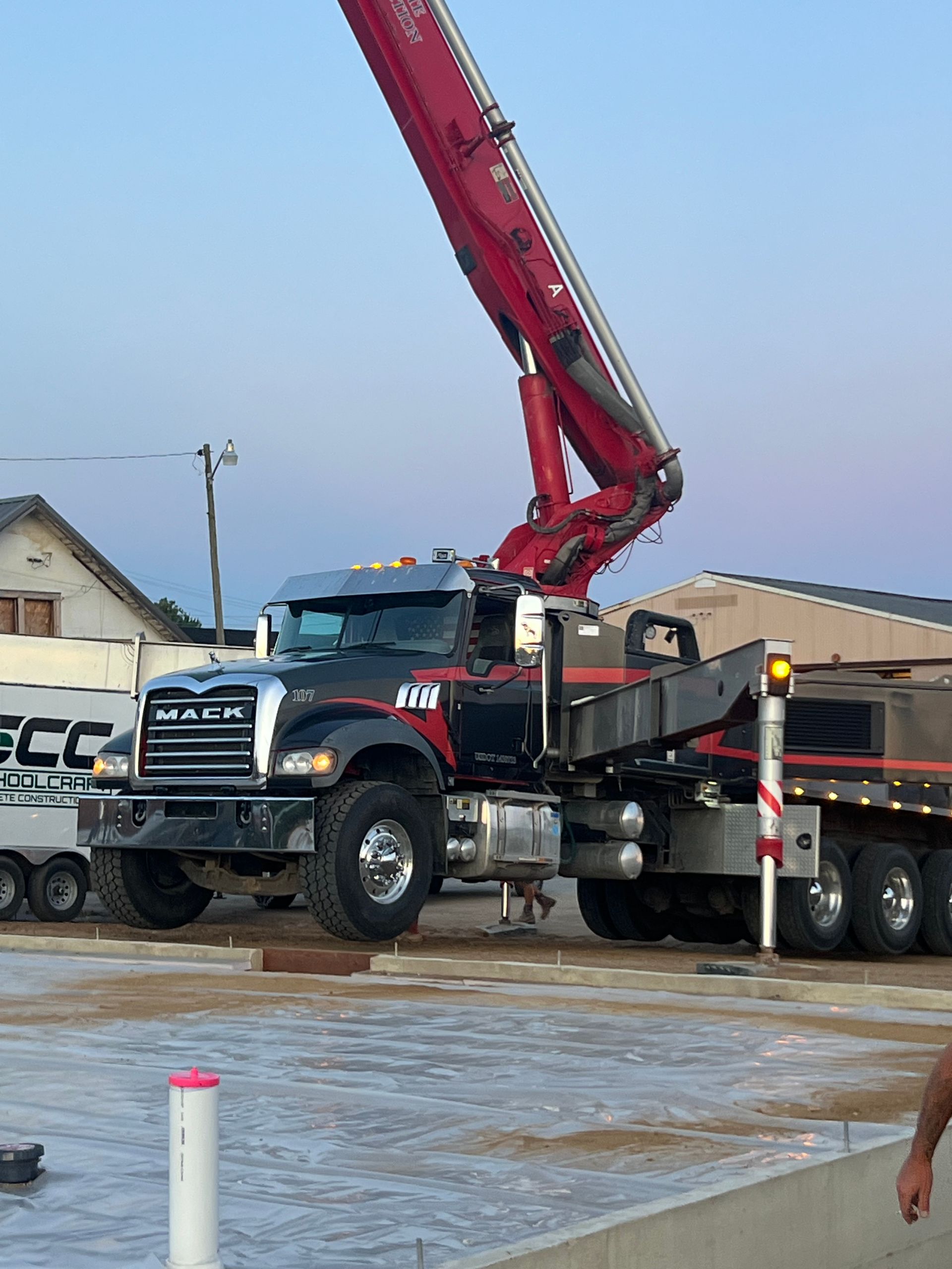 Red concrete pump truck pouring on a site, with another truck parked beside it.