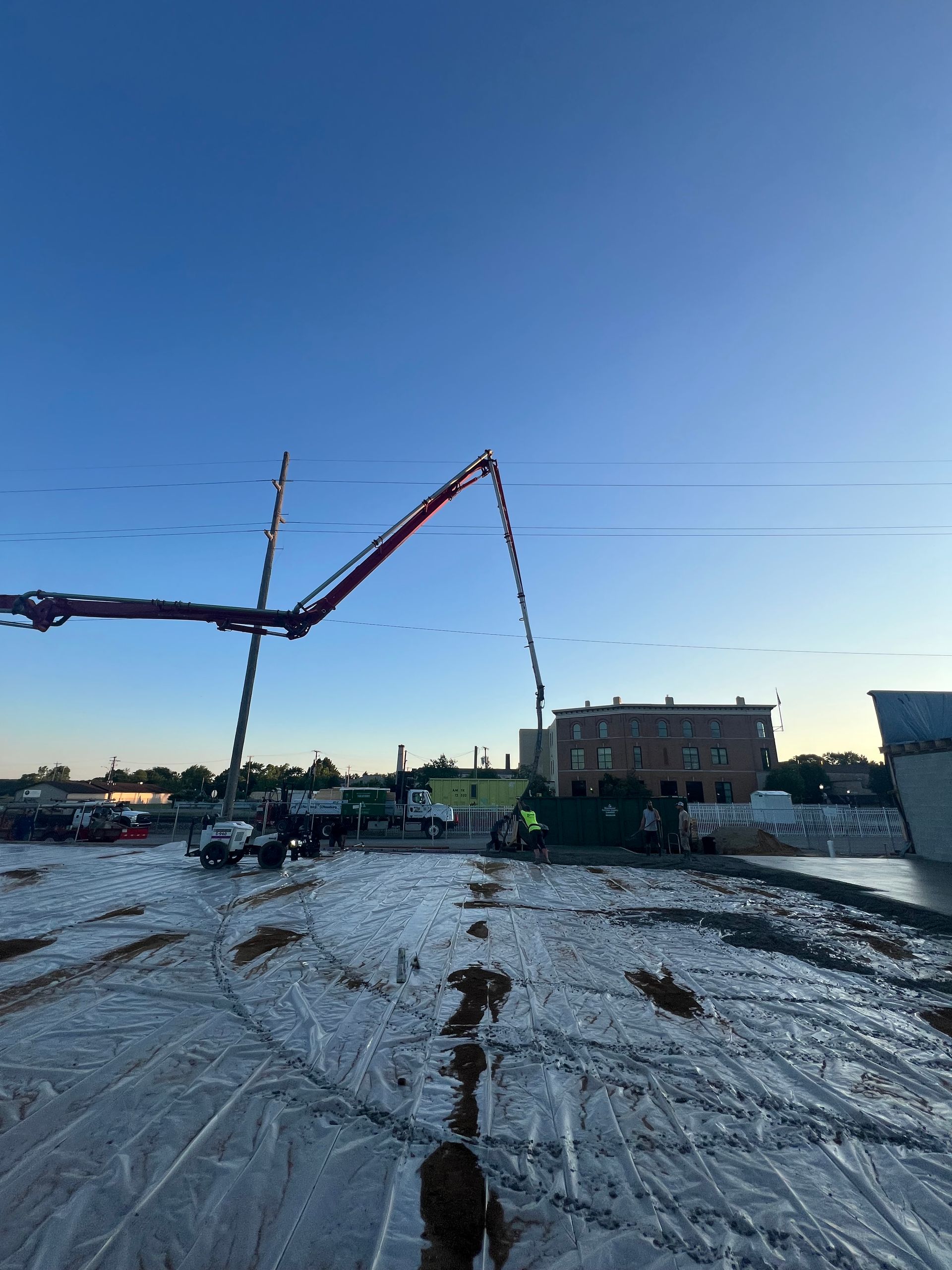 Concrete pump trucks pouring on a snowy construction site at dusk, with a building in the background