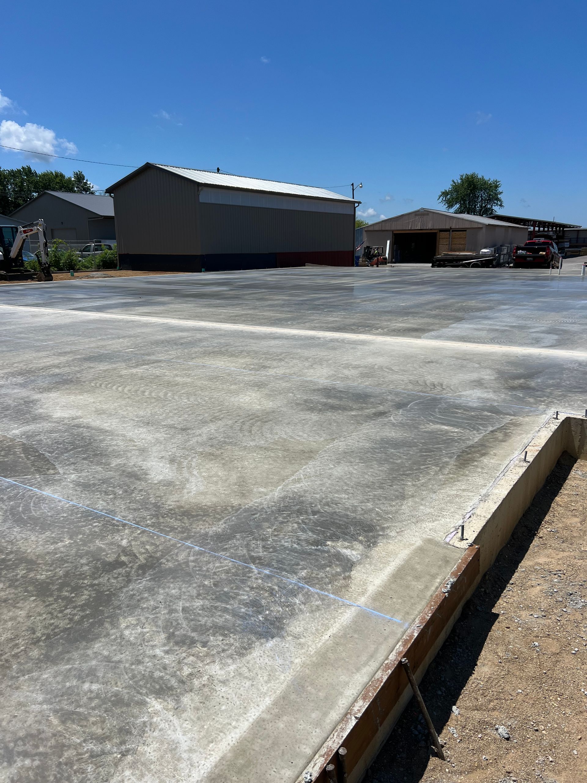 Empty concrete lot beside metal buildings under a clear blue sky