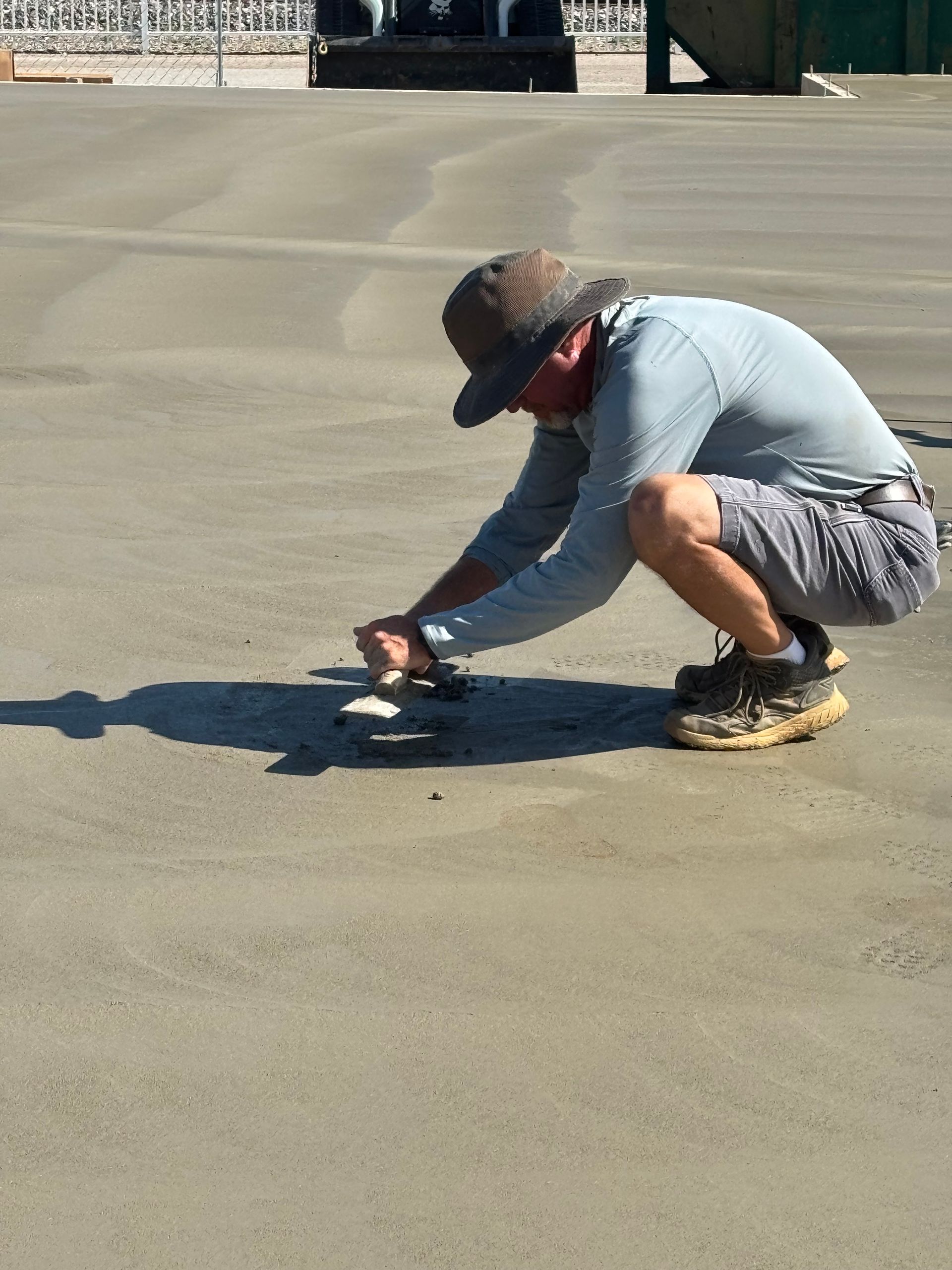 Person crouching on a sunlit concrete surface, adjusting a small object near a long shadow.