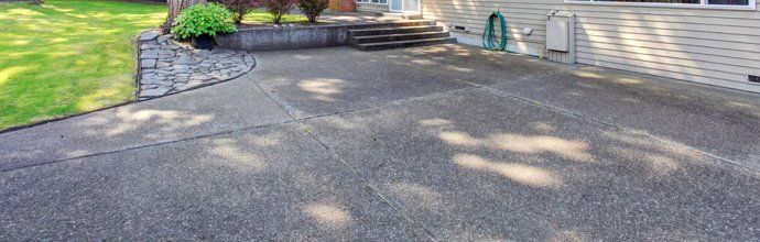 Driveway entrance with dark asphalt paving, stone edging, and potted plants by a house steps
