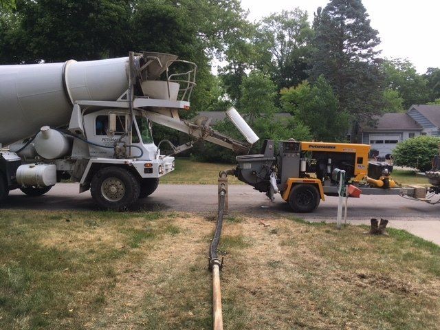 Cement mixer truck pouring concrete into a yellow pump truck on a suburban driveway