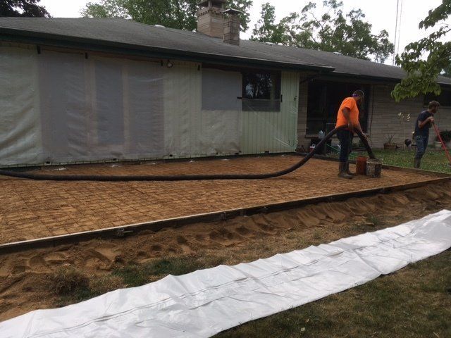 Driveway with gray pavers, white gravel strip, small green shrubs, and a short light post near a garage