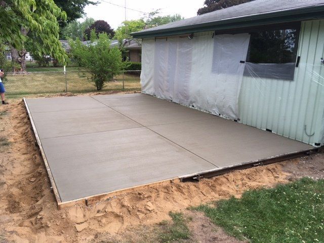 New concrete patio slab beside a house, bordered by dirt and grass