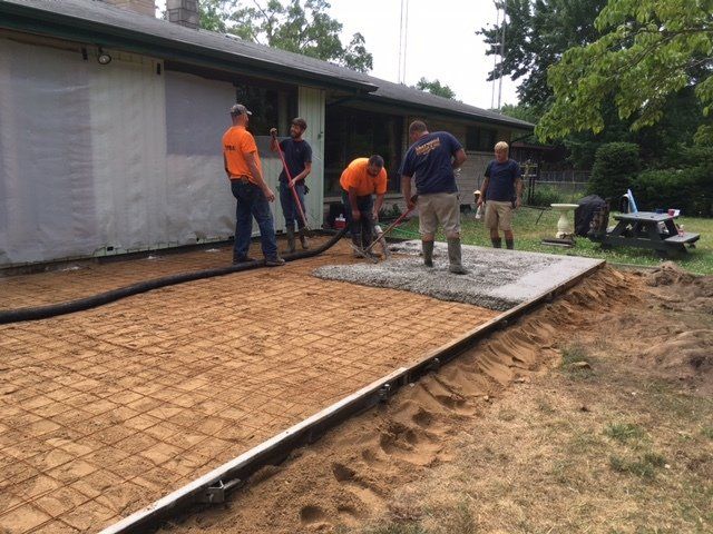 Workers smoothing concrete for a new driveway beside a house